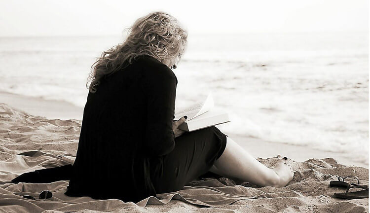 Kvinna sitter på strand och läser en bok